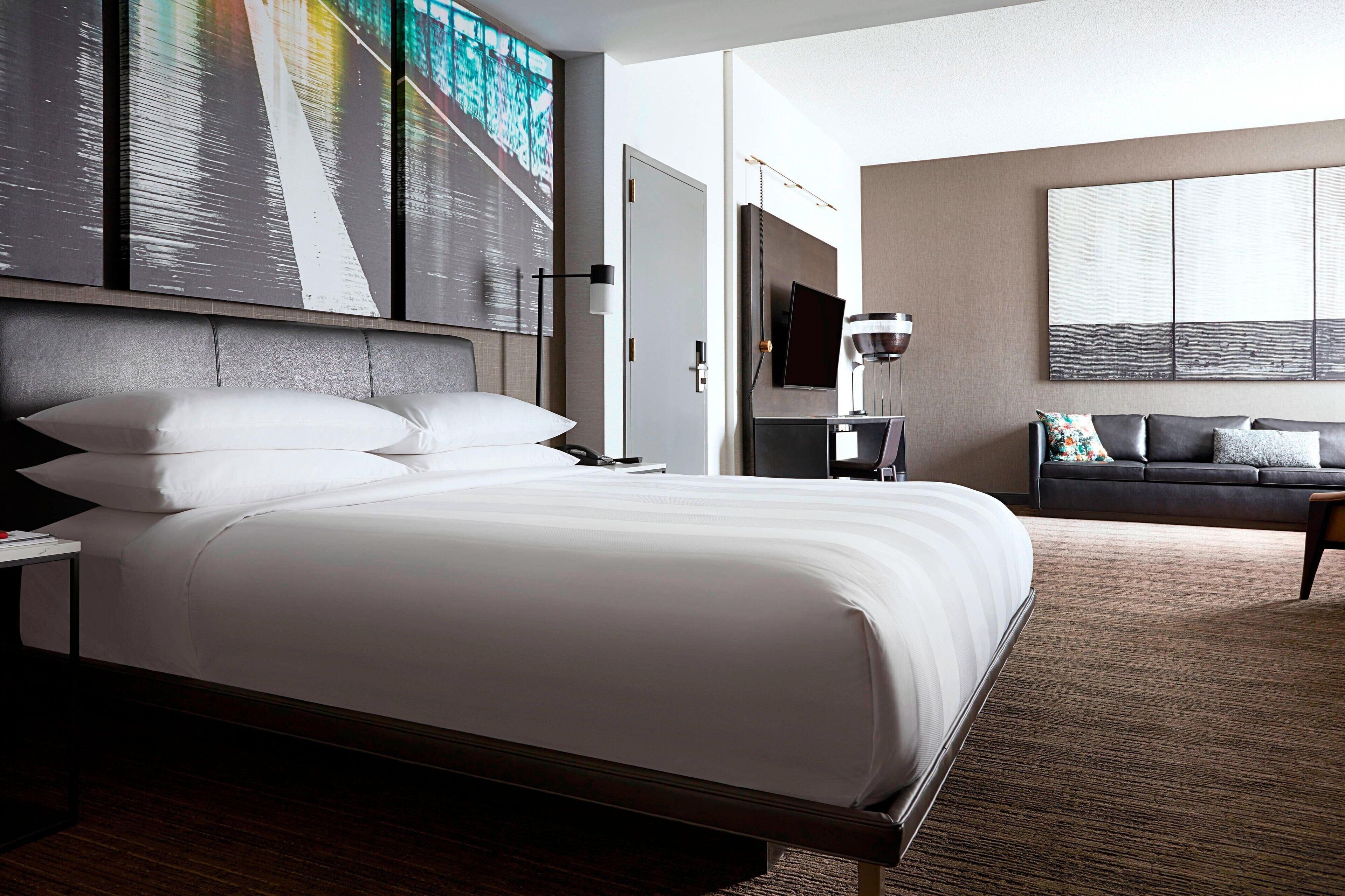 Une chambre d’hôtel moderne avec un grand lit, un canapé, une télévision et des œuvres d’art accrochées aux murs.