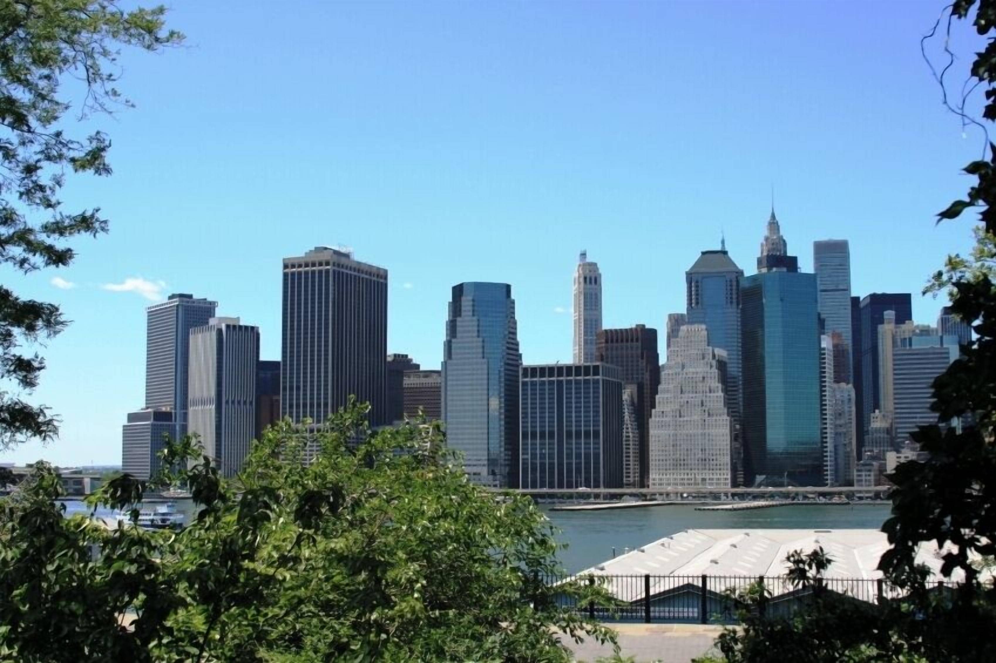 A city skyline with modern high-rise buildings, a body of water, and a fenced area in the foreground.