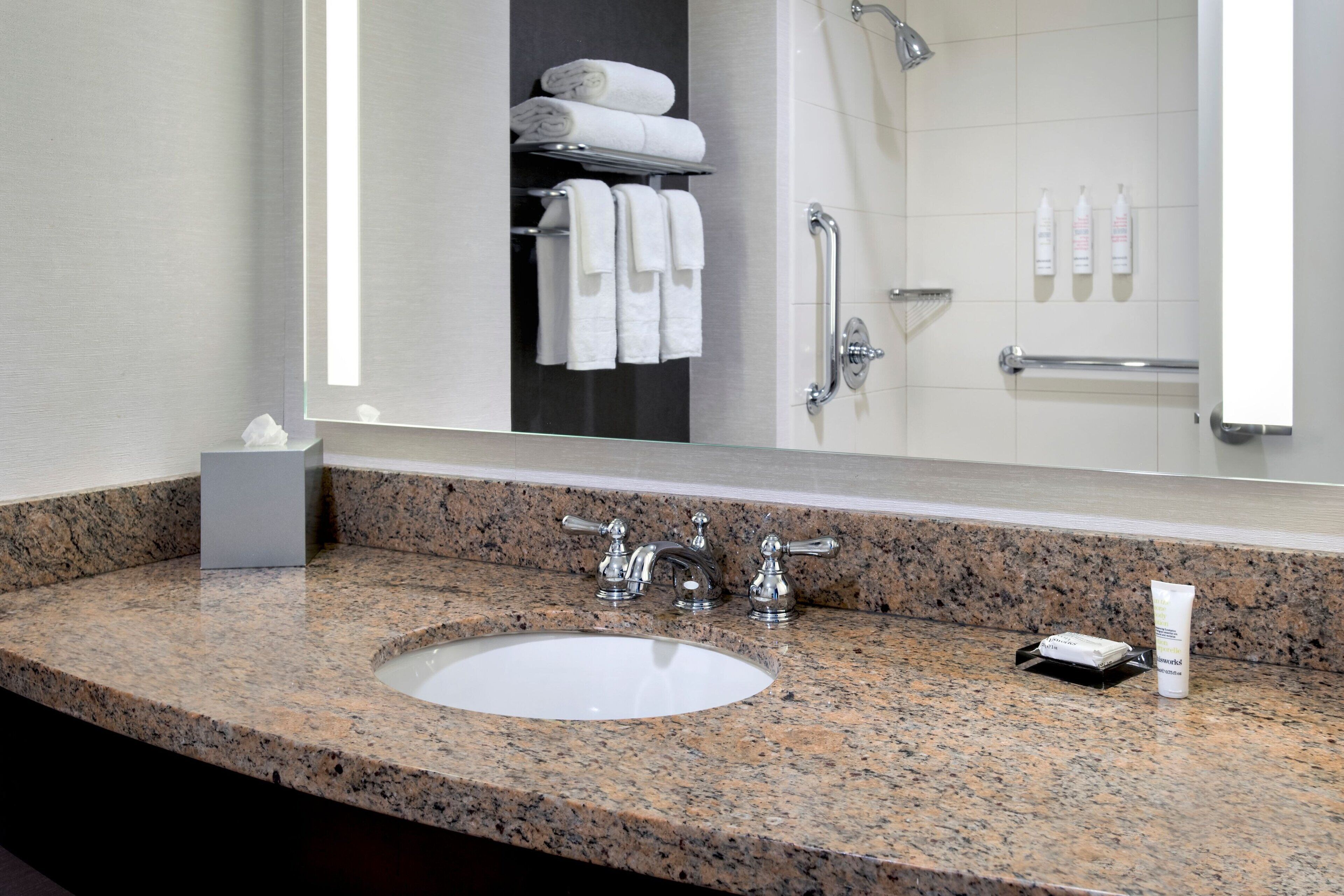 A bathroom with a granite countertop, a white sink, a mirror, and a towel rack with folded towels.
