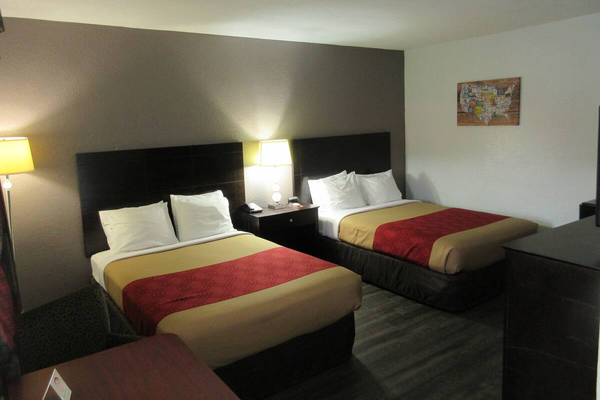 Une chambre d’hôtel avec deux lits, chacun doté d’une tête de lit, de tables de chevet, de lampes et d’une couvre-lit rouge et beige.
