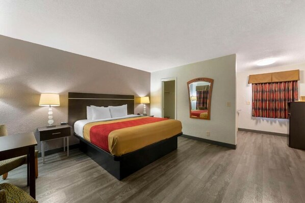 Una habitación de hotel con cama, mesitas de noche, escritorio, silla, espejo y armario.