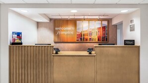 A hotel reception desk with a 'Welcome to Hampton' sign, a digital kiosk, and a 'Hilton Honors' sign. - Hampton Inn White River Junction (White River Junction)