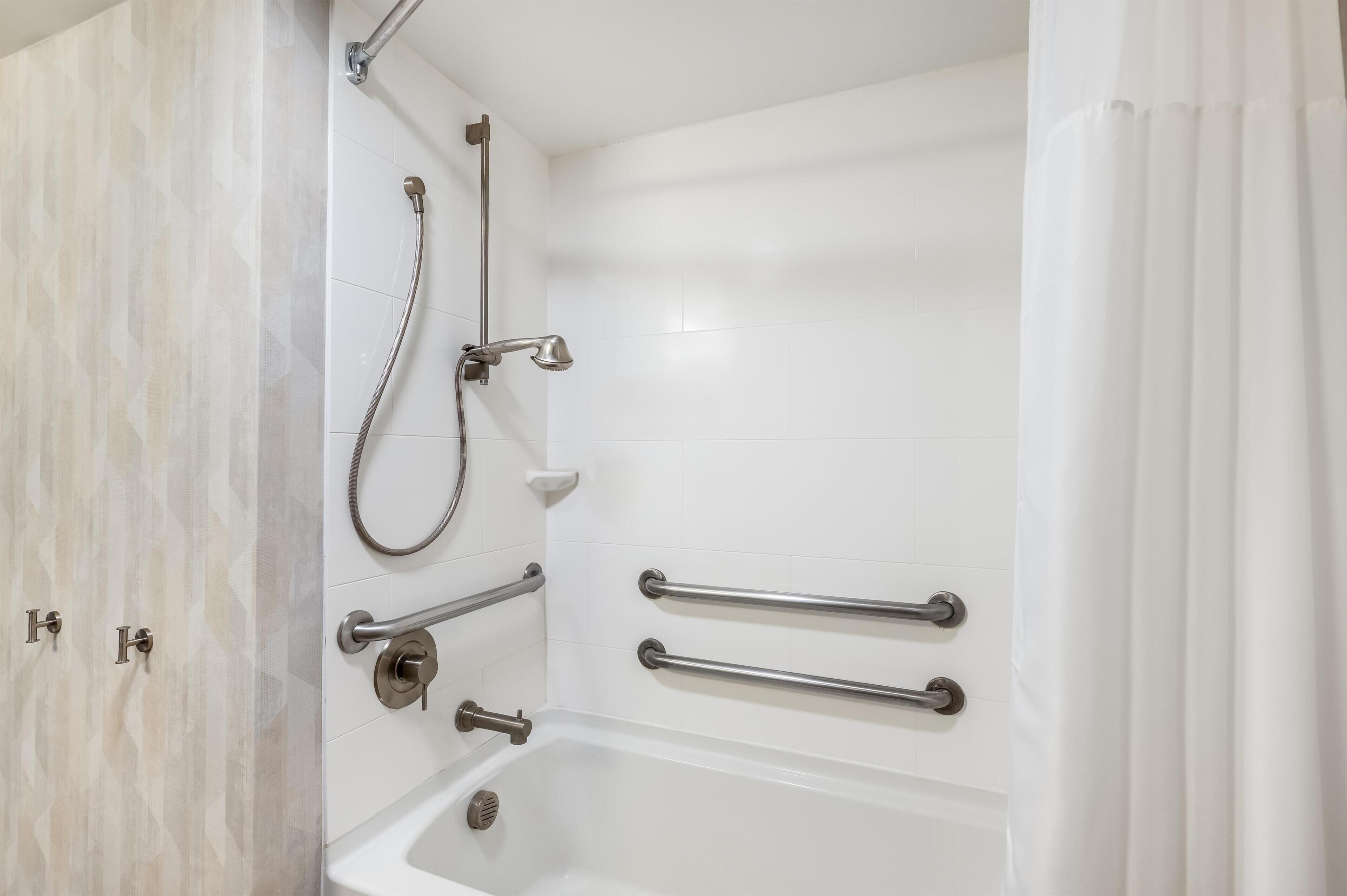 A bathroom with a bathtub, a shower, and grab bars.