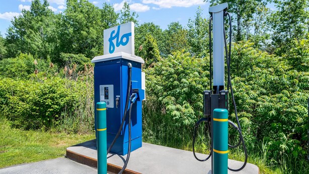A blue electric vehicle charging station with a sign, surrounded by greenery. - Hampton Inn White River Junction (White River Junction)