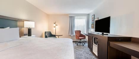 Habitación de hotel con una cama grande, un escritorio con televisión de pantalla plana, una silla y una lámpara.