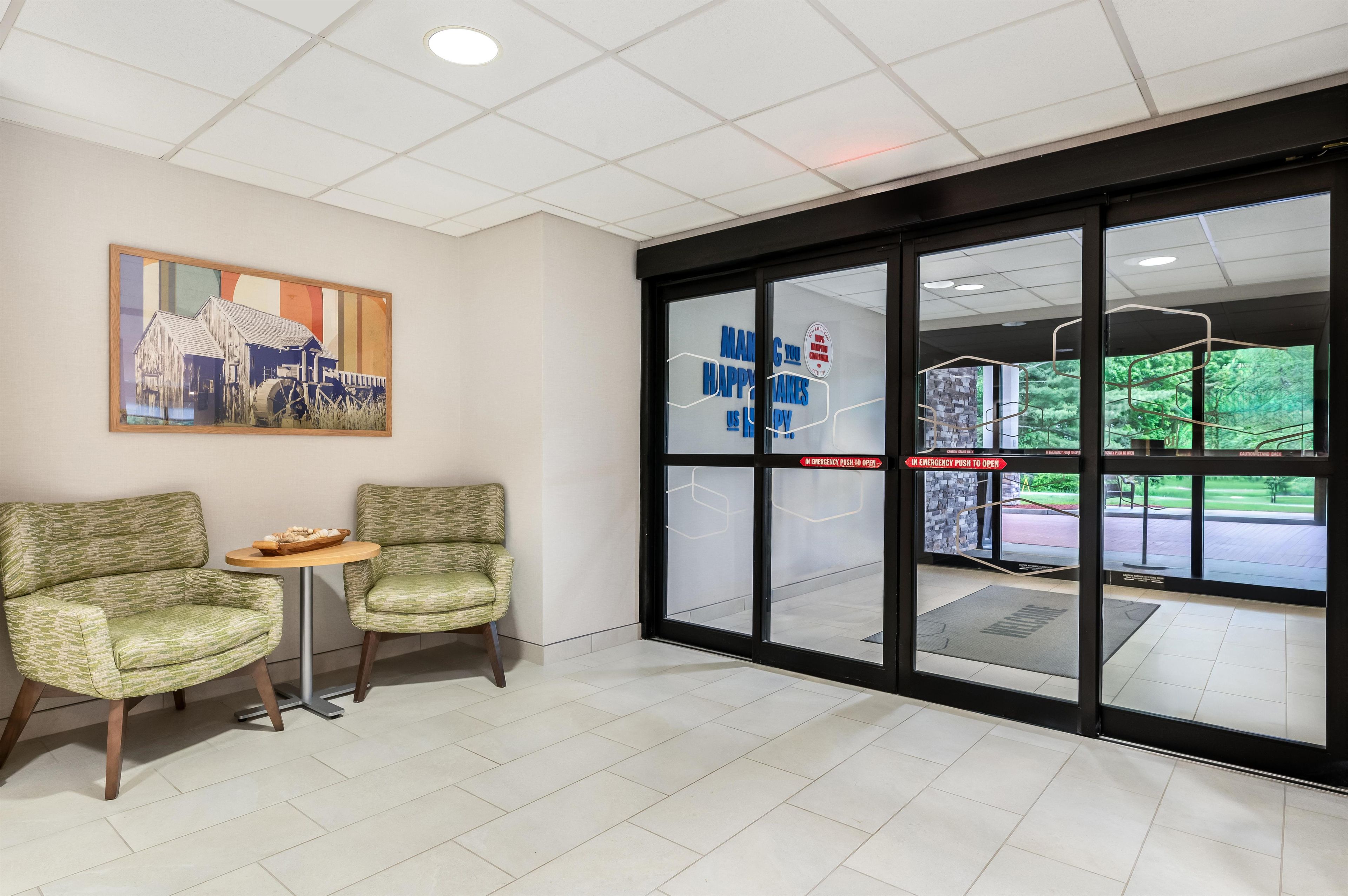 A reception area with two chairs, a small table, a painting on the wall, and a glass door with emergency instructions.