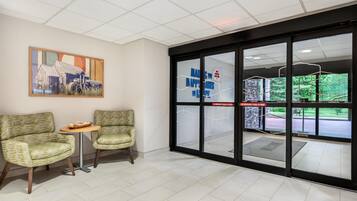 A reception area with two chairs, a small table, a painting on the wall, and a glass door with emergency instructions.