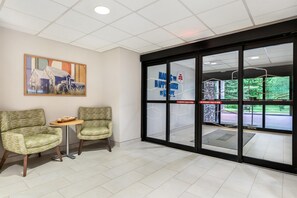 A reception area with two chairs, a small table, a painting on the wall, and a glass door with emergency instructions. - Hampton Inn White River Junction (White River Junction)