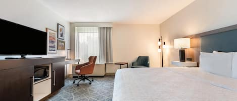 A hotel room with a bed, a desk, a chair, a television, and a window with curtains.