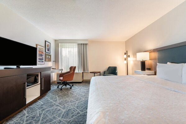 A hotel room with a bed, a desk, a chair, a television, and a window with curtains. - Hampton Inn White River Junction (White River Junction)