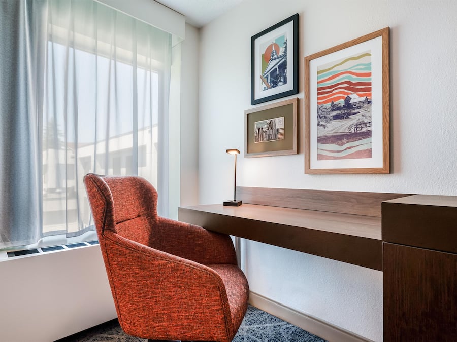 A hotel room with a desk, a chair, and three framed artworks on the wall.