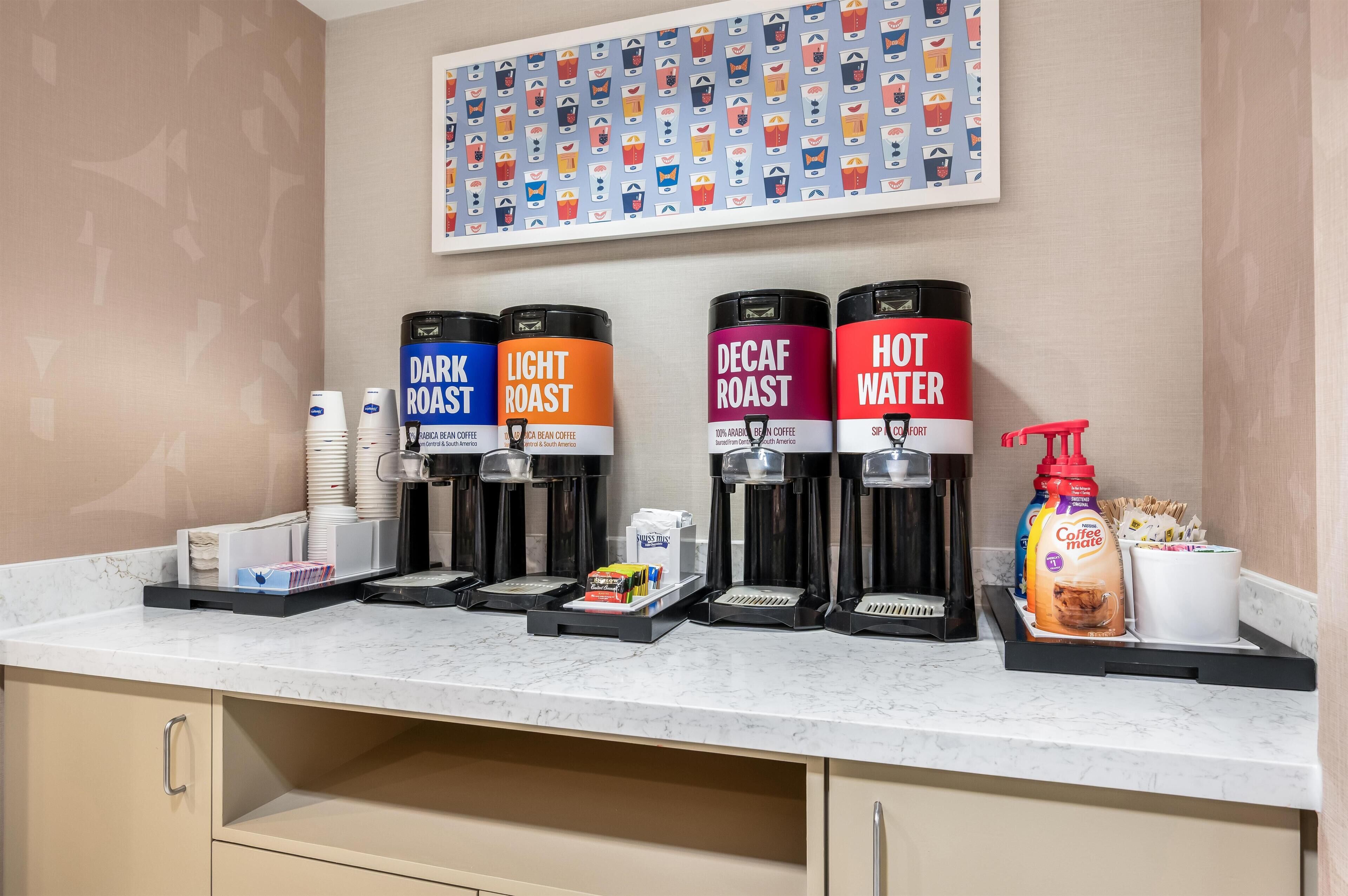 Una estación de café con cuatro dispensadores etiquetados como: TUESTA OSCURA, TUESTA CLARA, DESCAFEINADO y AGUA CALIENTE.