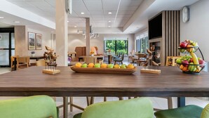A spacious dining area with a long wooden table, multiple chairs, and a fruit display. - Hampton Inn White River Junction (White River Junction)