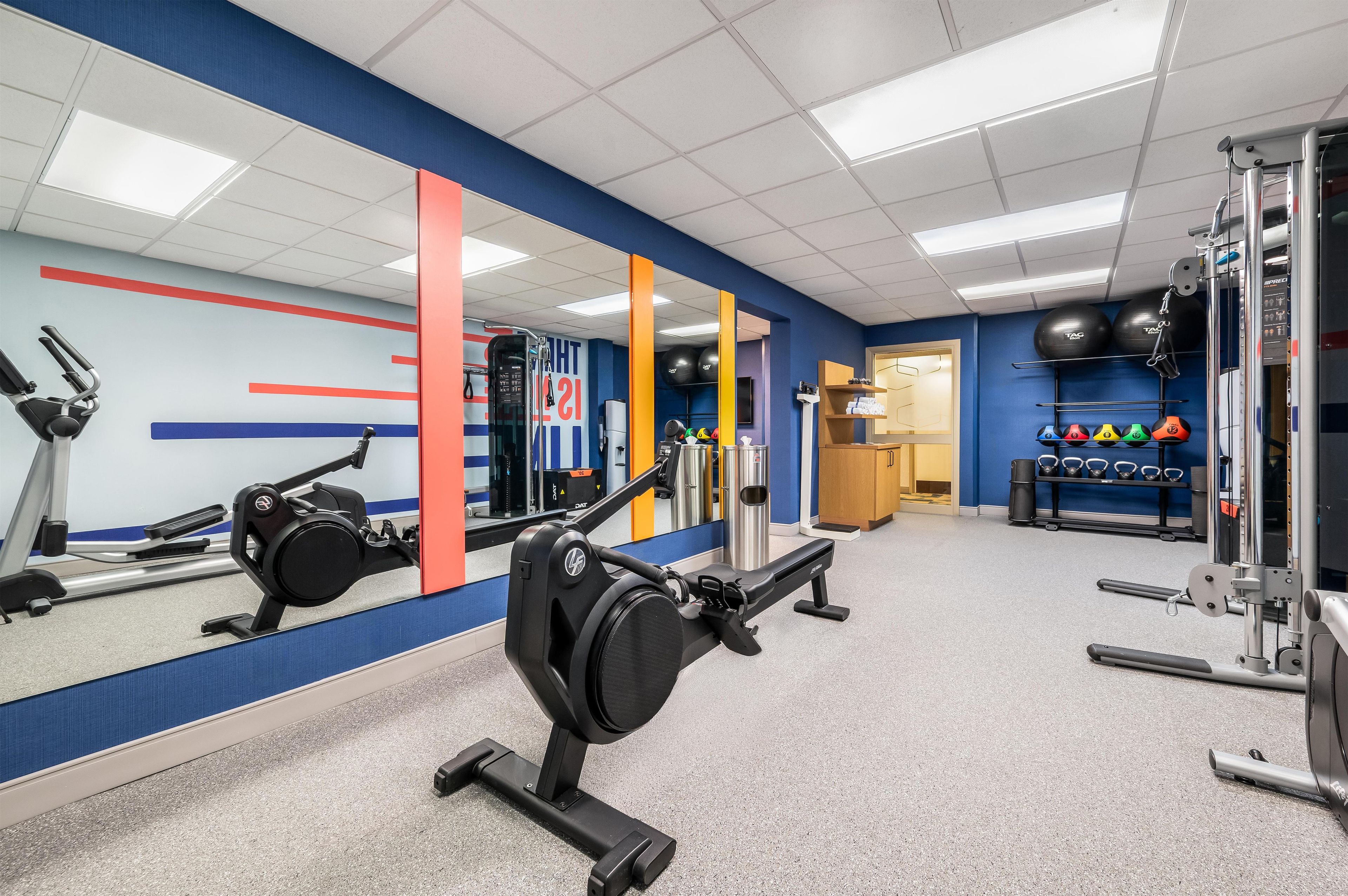 Un gimnasio con equipo de ejercicio, un espejo y una pared con diseño rojo y azul.