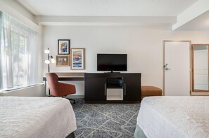 Quarto de hotel com duas camas, uma escrivaninha com televisão de ecrã plano, uma cadeira e um guarda-roupa.