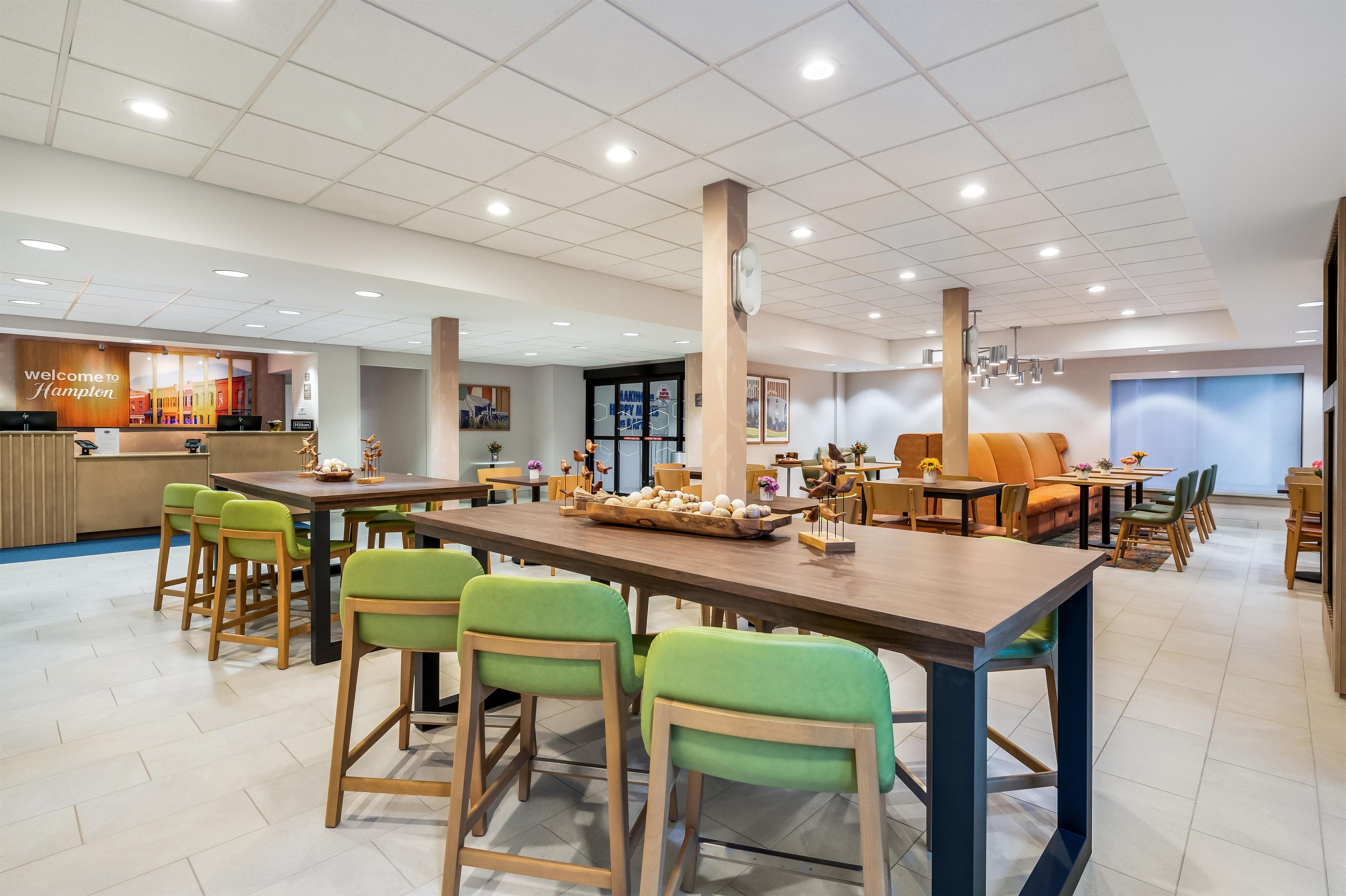 A hotel lobby with a reception desk, seating areas, and a large dining table with chairs.