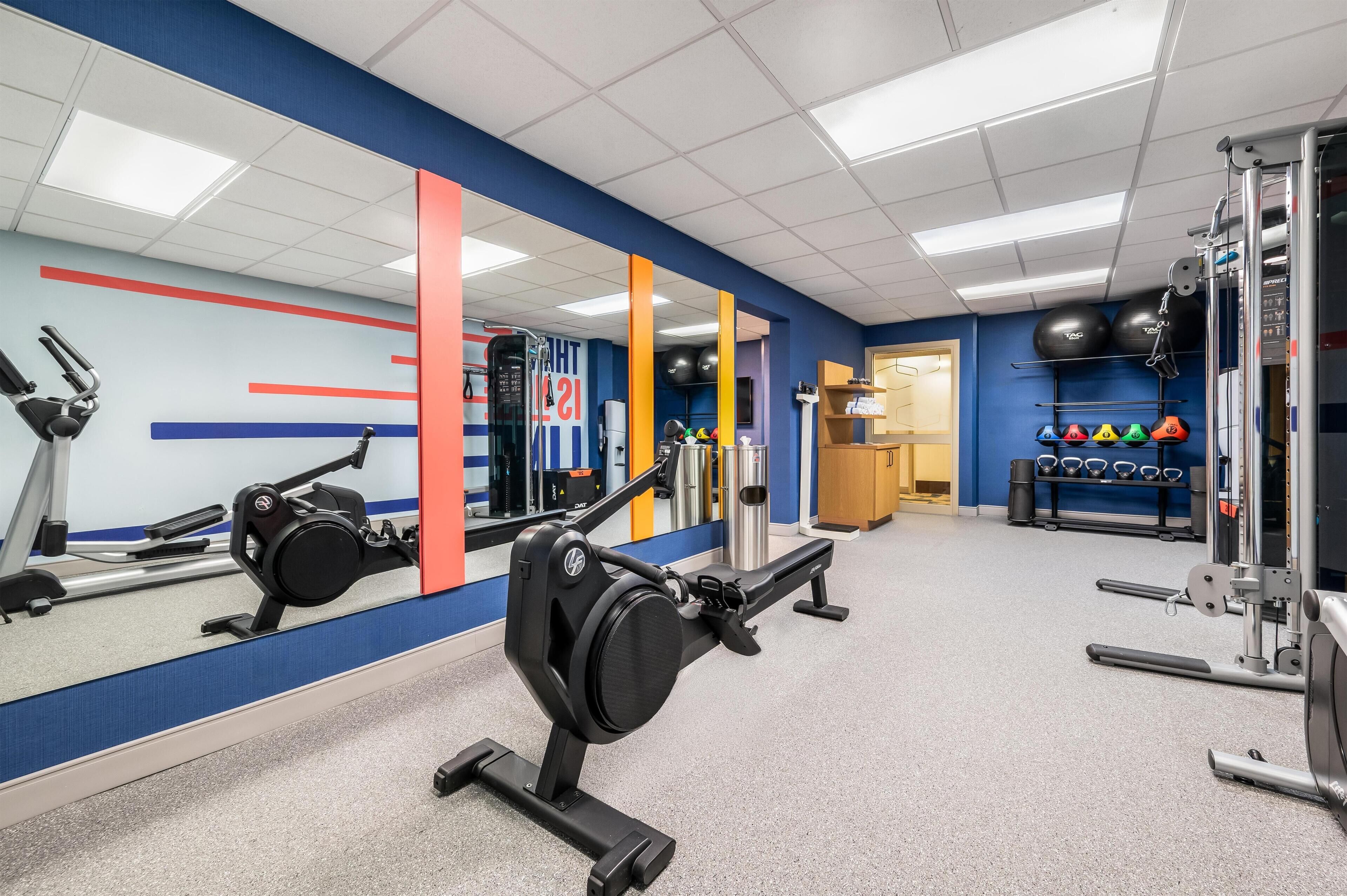 Un gimnasio con equipo de ejercicio, un espejo y una pared con diseño rojo y azul.
