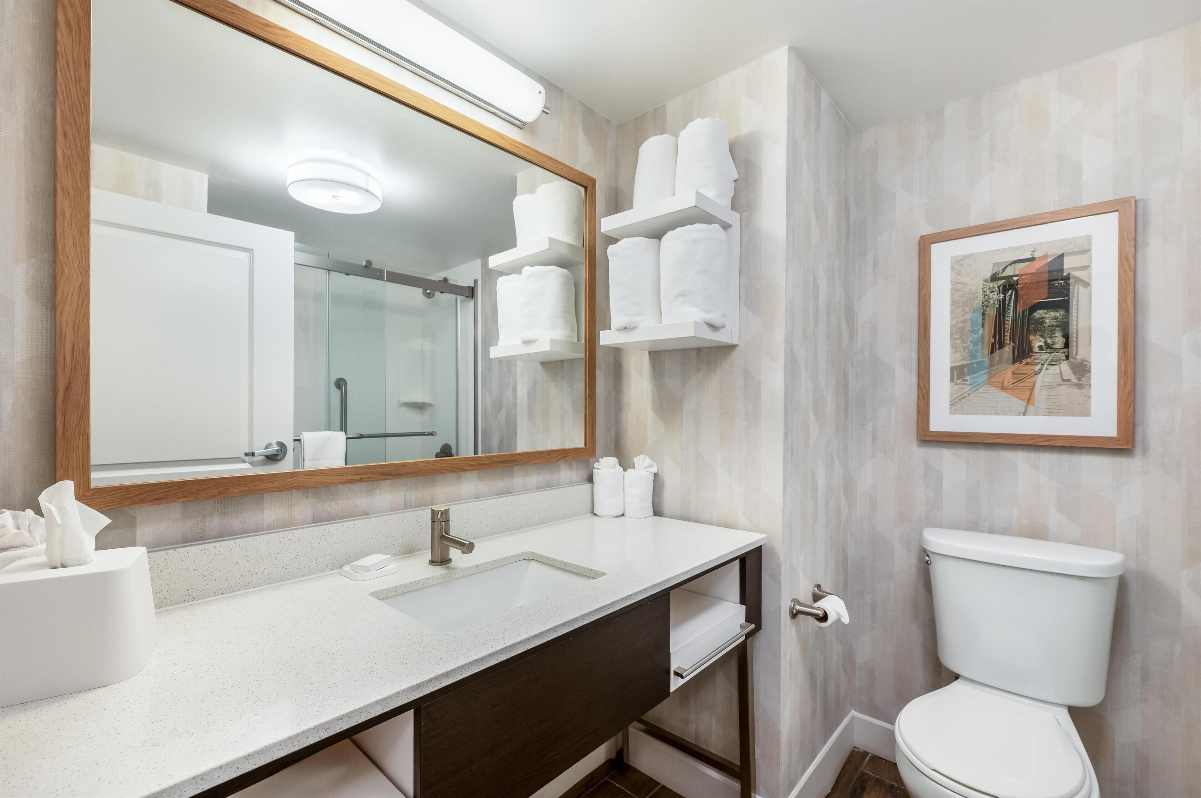 A bathroom with a large mirror, two sinks, a toilet, and a framed picture on the wall.