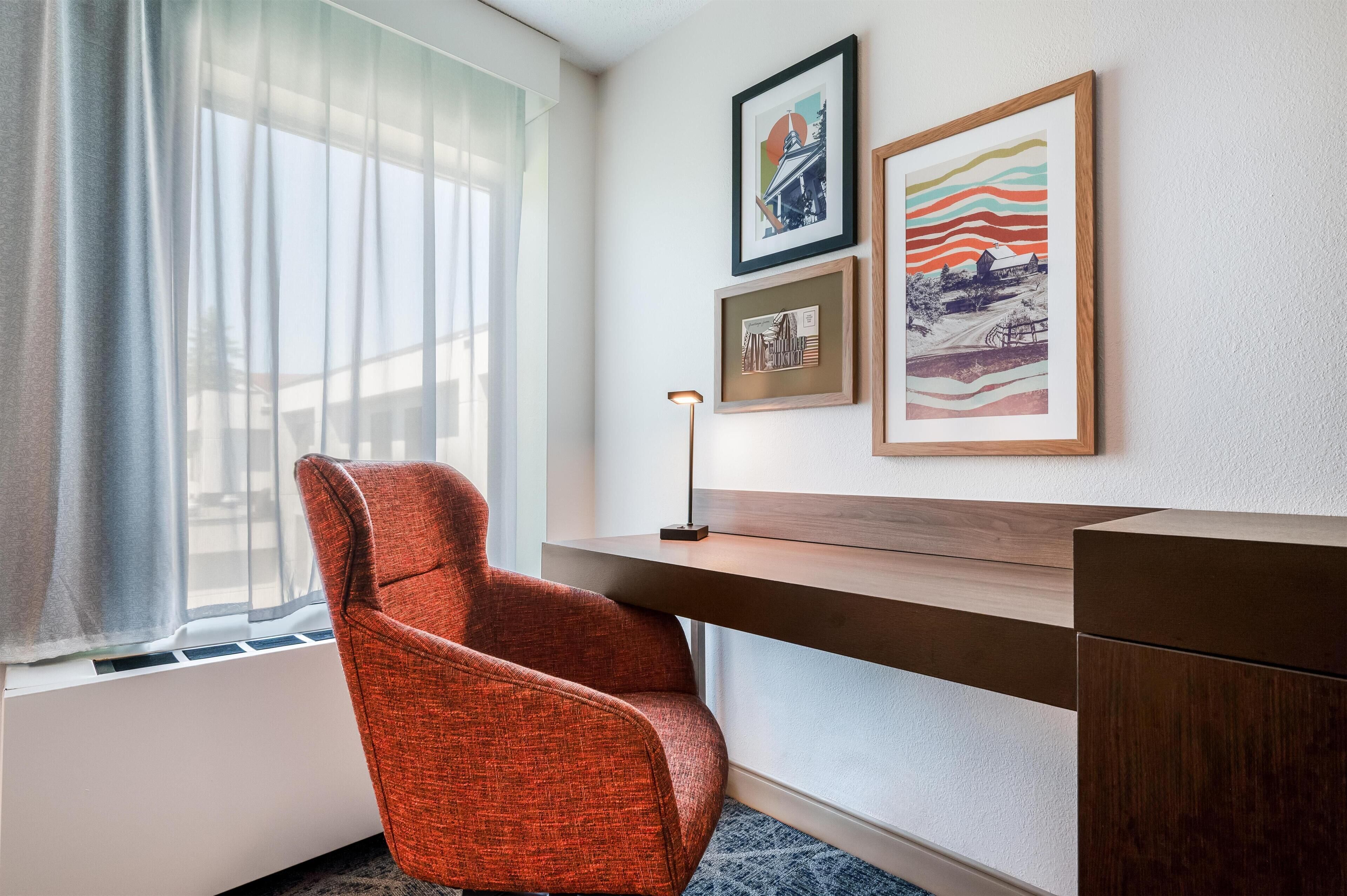 Habitación de hotel con escritorio, una silla y tres cuadros en la pared.