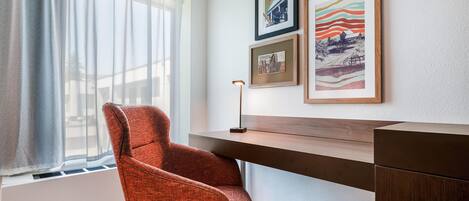 Habitación de hotel con escritorio, una silla y tres cuadros en la pared.