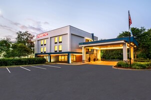 Un hotel Hampton Inn con una fachada moderna, un acceso cubierto y un estacionamiento.
