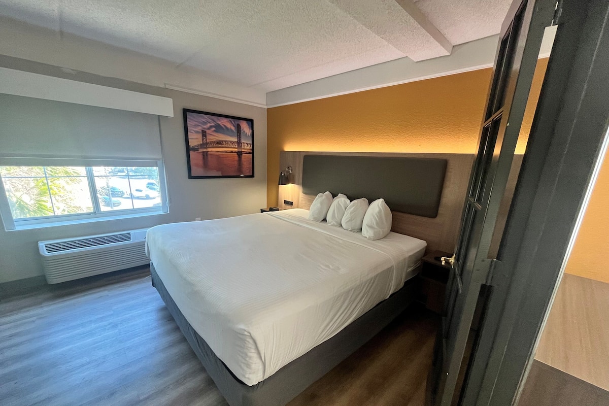 A modern bedroom with a large bed, a window with a view, and a mounted picture on the wall.