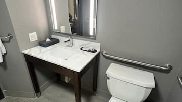 Een badkamer met een wit wastafel, een spiegel, een toilet en een prullenbak.