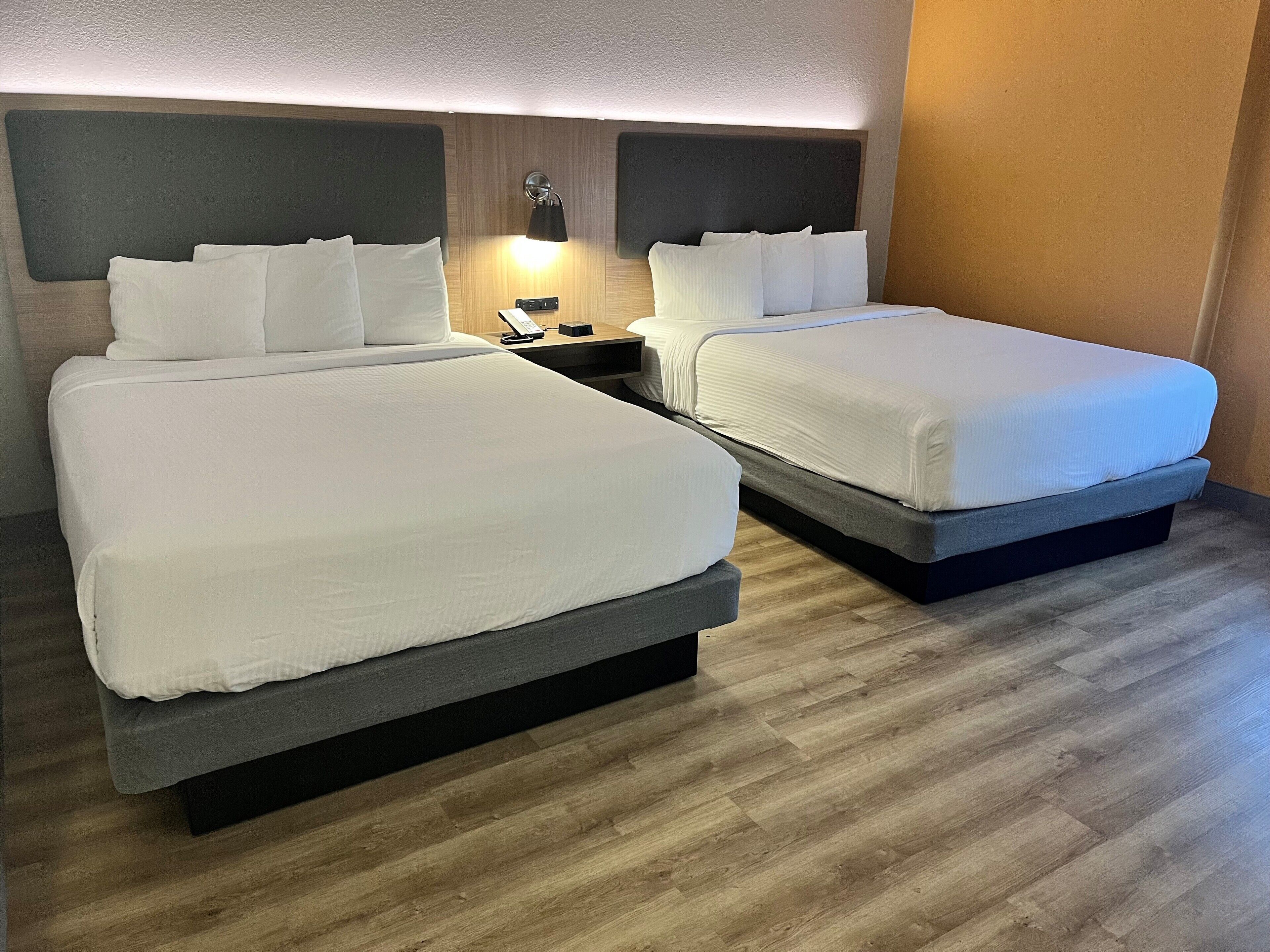 Une chambre d’hôtel avec deux lits, une table de chevet avec une lampe et un téléphone fixé au mur.