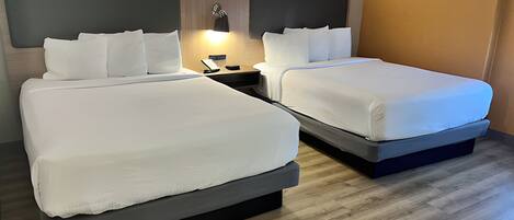 A hotel room with two beds, a nightstand, and a wall-mounted lamp.