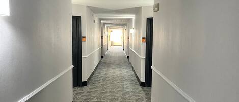 A long, narrow hotel corridor with a patterned carpet, white walls, and doors on both sides.