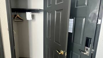 Un couloir avec une porte en bois foncé, un porte-manteau avec des cintres et un mur de couleur claire.