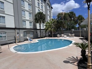 A swimming pool with lounge chairs and palm trees, surrounded by a building with multiple windows and a covered patio area. - La Quinta Inn & Suites by Wyndham Jacksonville Butler Blvd (Jacksonville)
