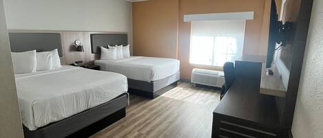 A hotel room with two beds, a desk, a flat-screen TV, and a window with blinds.