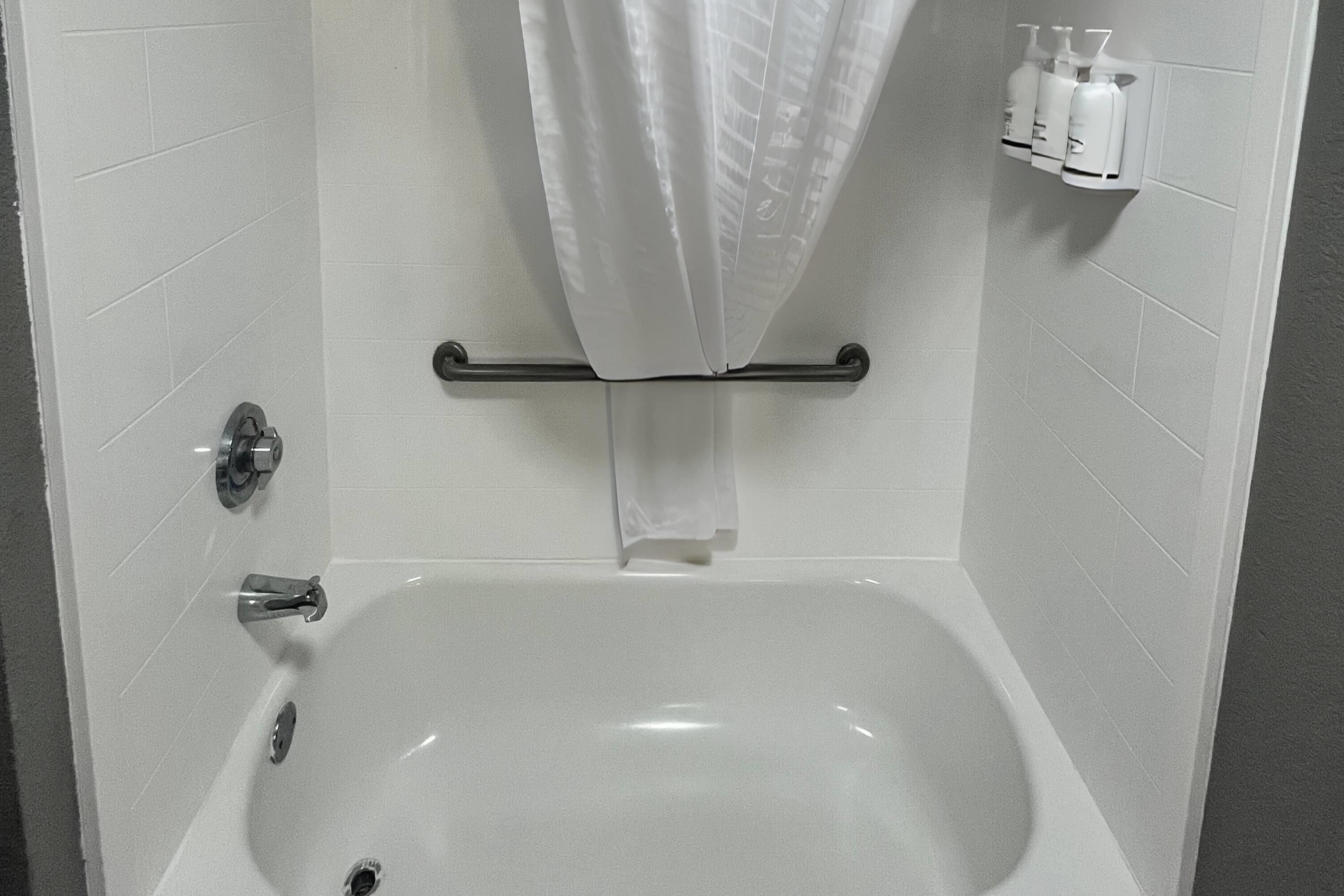 Et badeværelse med badekar, bruseforhæng, et håndklædestativ og toiletartikler på en hylde.