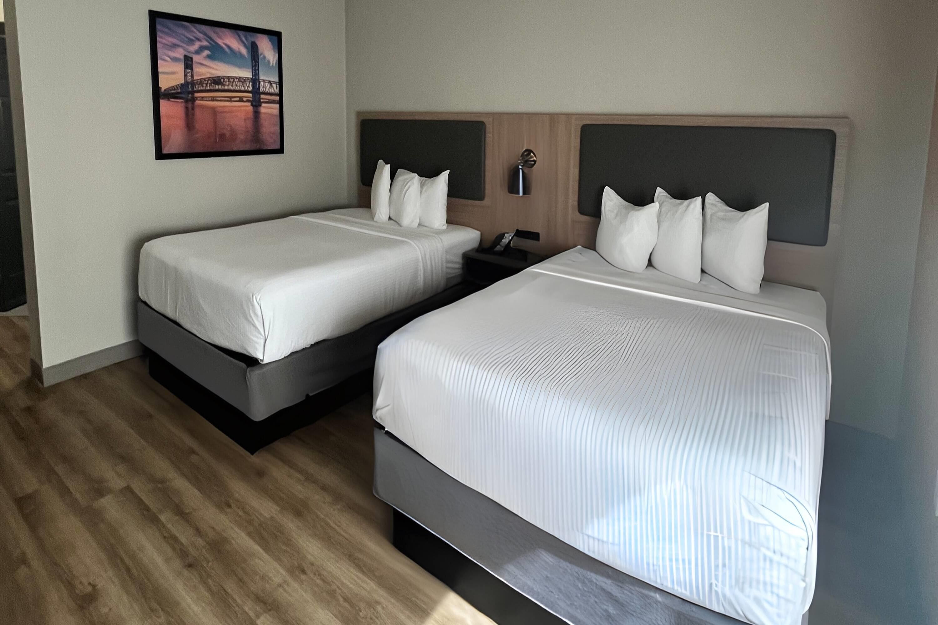 A hotel room with two beds, a nightstand, a wall-mounted lamp, and a framed picture of a bridge.
