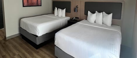 A hotel room with two beds, a nightstand, a wall-mounted lamp, and a framed picture of a bridge.
