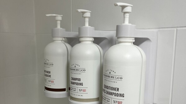 Three bottles of Old Town Woodbury & Co. toiletries on a white tiled wall.