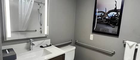 A bathroom with a white sink, mirror, and toilet. There is a handrail on the wall and a towel rack with towels.