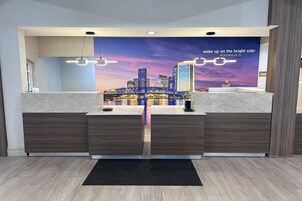 Bancada de recepção de hotel com um mural da paisagem urbana, design moderno e um tapete de entrada preto.