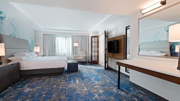 Una habitación de hotel con cama, escritorio, silla, televisor y un espejo grande.