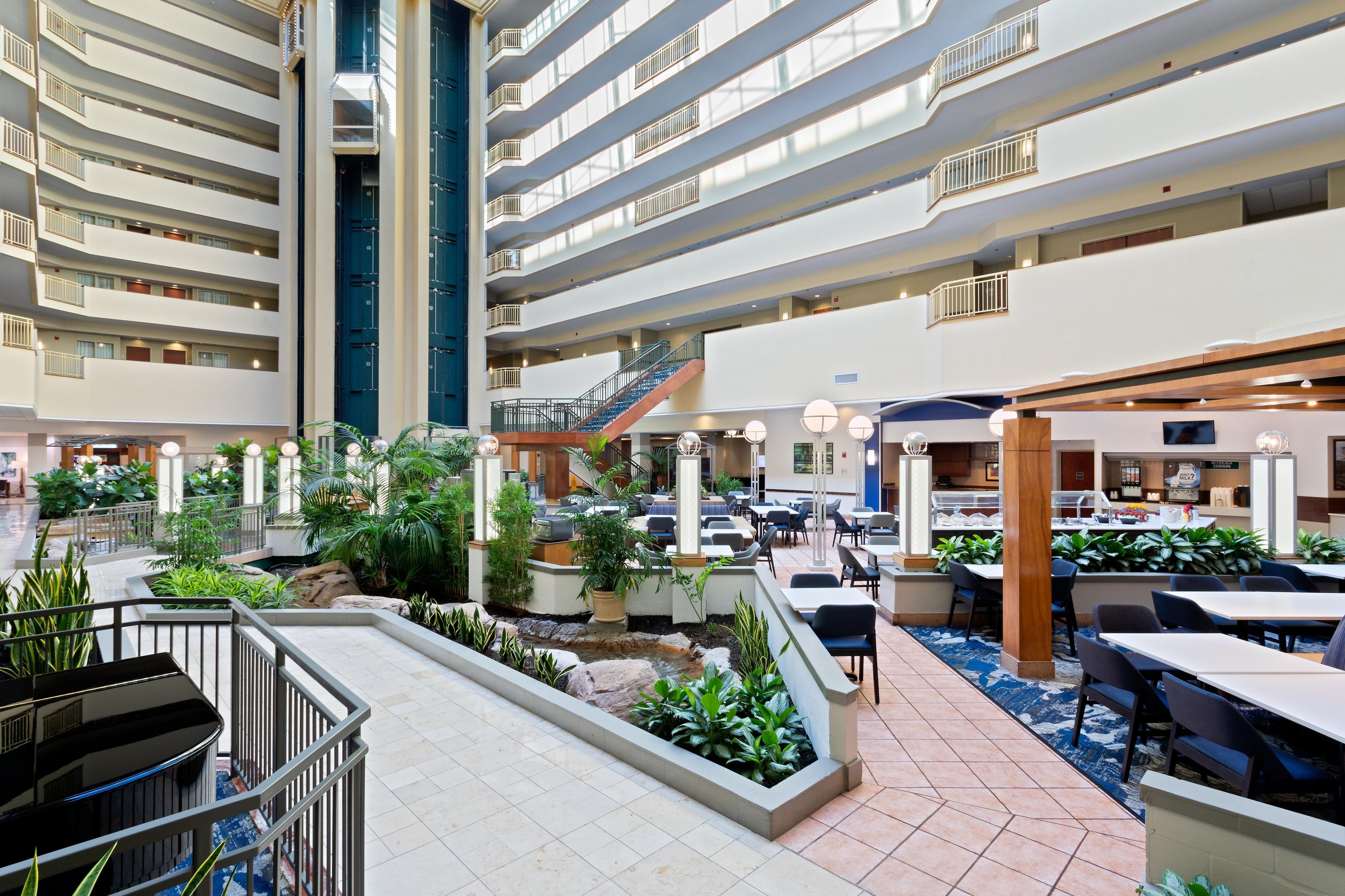 A multi-level hotel lobby with a central atrium, multiple dining areas, and a staircase connecting the floors.