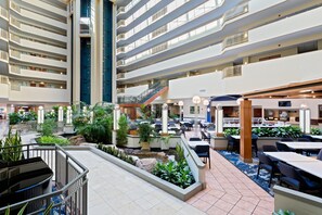 Un lobby de hotel de varios niveles con un atrio central, varias zonas de comedor y una escalera que conecta los pisos.