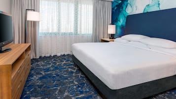 Una habitación de hotel con cama, televisión, escritorio y ventana con cortinas.