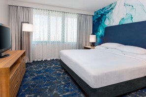 Una habitación de hotel con cama, televisión, escritorio y ventana con cortinas.