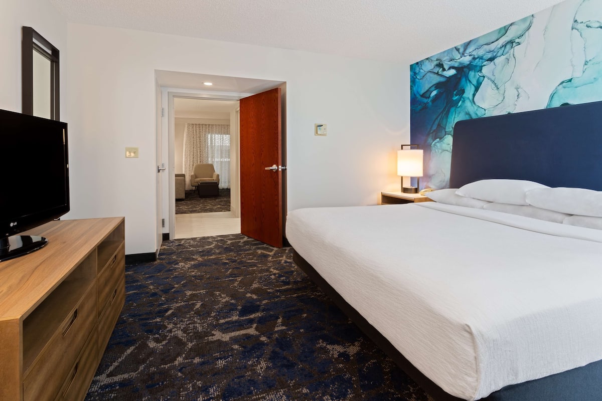 Ein Hotelzimmer mit Bett, Fernseher, einem Gemälde und Teppichboden.