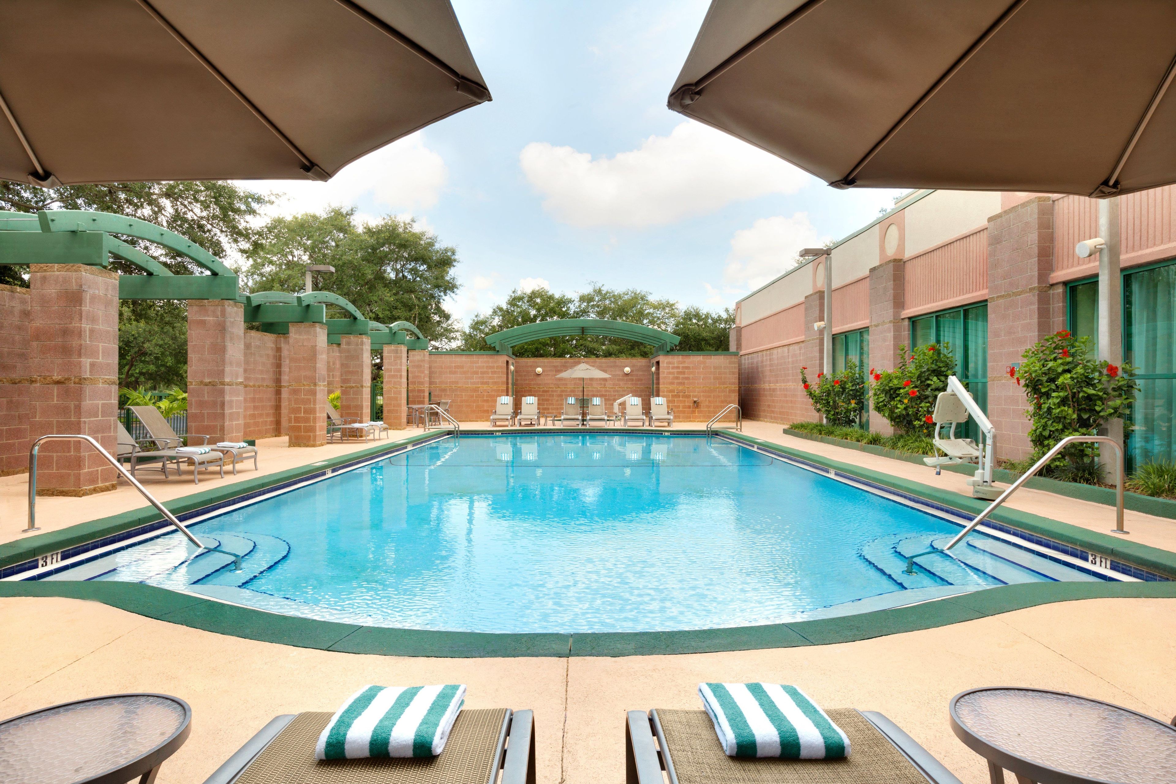 A swimming pool with lounge chairs and umbrellas, surrounded by brick walls and greenery.