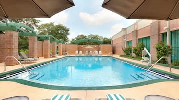 A swimming pool with lounge chairs and umbrellas, surrounded by brick walls and greenery.