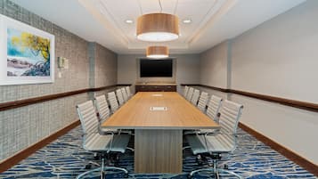 A conference room with a long table, chairs, a large painting, and a mounted TV.