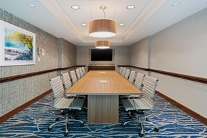 A conference room with a long table, chairs, a large painting, and a mounted TV.