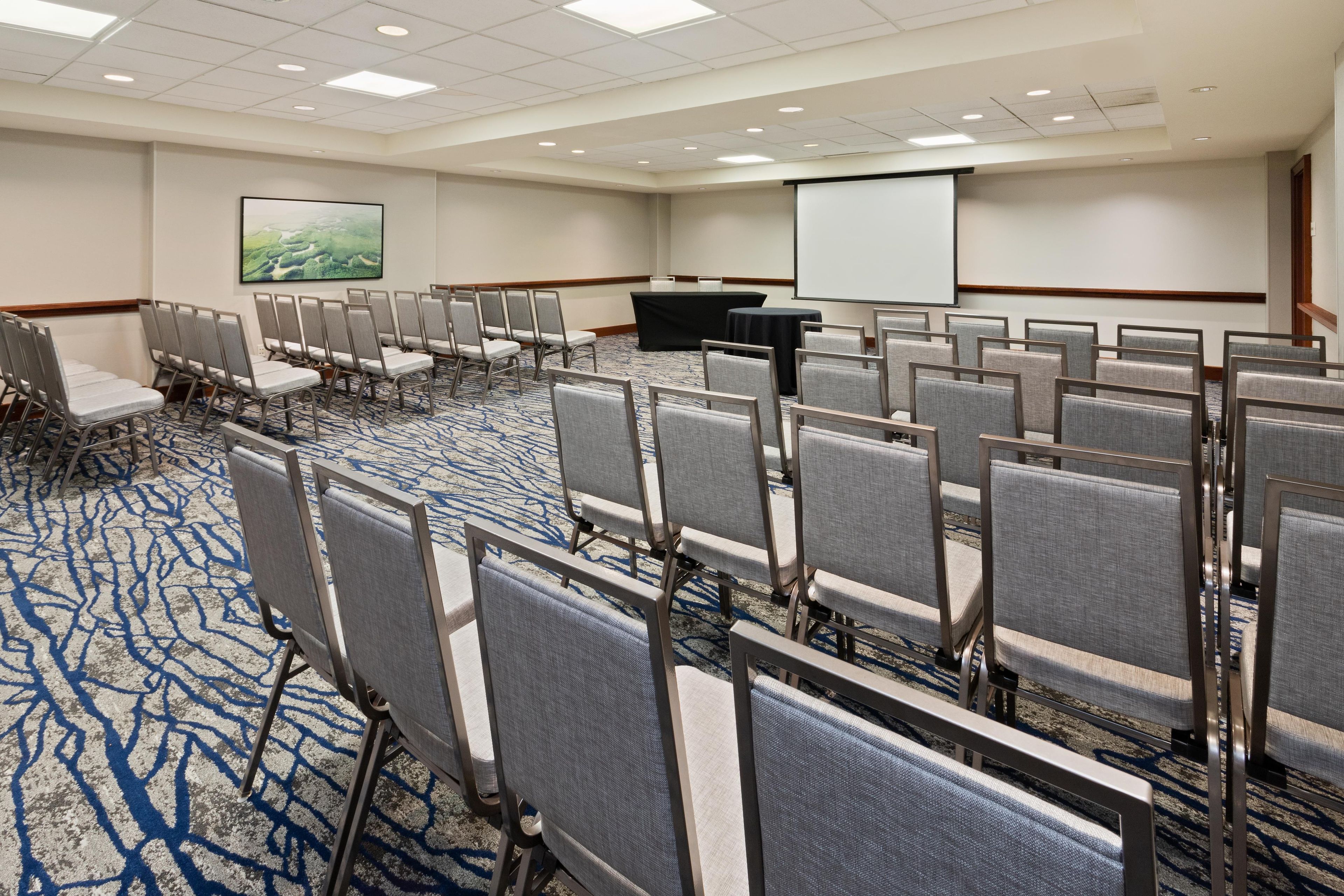 A conference room with rows of chairs, a projector screen, and a presentation screen.
